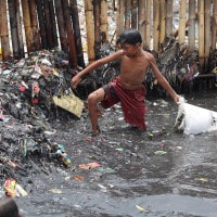Un bambino fa il bagno tra i rifiuti a Jakarta, Indonesia