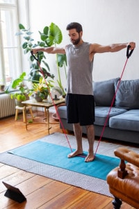 Un uomo che si esercita con la fascia elastica a casa seguendo un tutorial online durante l'isolamento per Covid-19
